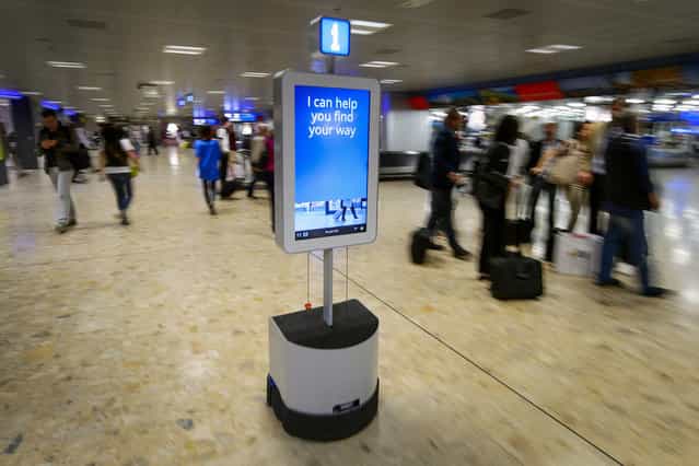 A robot helps passengers to find their way through the baggage claim area of the Geneva International Airport, on June 13, 2013. Geneva airport is using the autonomous robot to accompany travelers to a dozen destinations such as trolleys, ATM, lost luggage room, showers or toilets. (Photo by Fabrice Coffrini/AFP Photo)