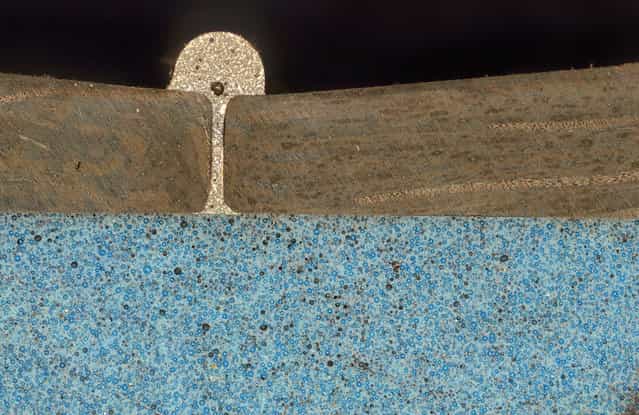 Image of Distinction: A 50x image showing a cross-cut through an assembly of two dark-brown fiber-reinforced composite pieces, which are bonded together with gray adhesive and back-filled with a blue mass of composite material, by Peter Pook, Composites Atlantic Ltd., Lunenburg, Nova Scotia. (Photo by Peter Pook)
