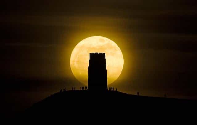 People stand beside St. Michaels Tower on Glastonbury Tor hill in England, watching the moon as it progresses across the sky at its closest point to the Earth in almost two decades