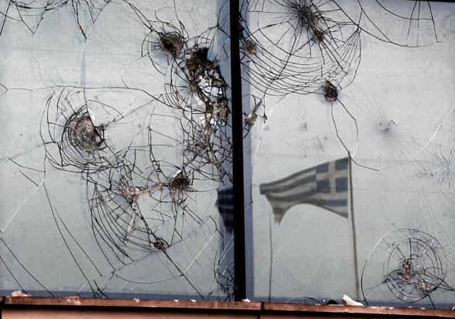 A Greek flag is reflected on the smashed windows of a bank in Athens.