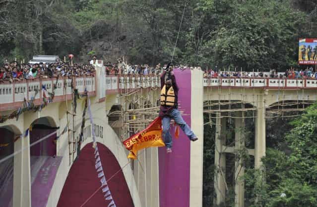 In this Sunday, April 28, 2013 photograph, people watch as Indian Sailendra Nath Roy attempts to cross Teesta river suspended from a zip wire attached to his ponytail moments before his death in Siliguri, West Bengal state, India. Roy who was named a Guinness World Record holder in 2011 for travelling the farthest distance on a zip wire using hair died during the stunt Sunday when he suffered a heart attack. (Photo by AP Photo)