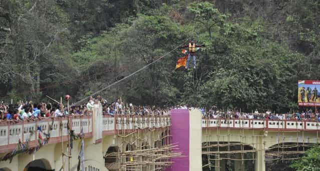 In this Sunday, April 28, 2013 photograph, people watch as Indian Sailendra Nath Roy attempts to cross Teesta river suspended from a zip wire attached to his ponytail moments before his death in Siliguri, West Bengal state, India. Roy who was named a Guinness World Record holder in 2011 for travelling the farthest distance on a zip wire using hair died during the stunt Sunday when he suffered a heart attack. (AP Photo)