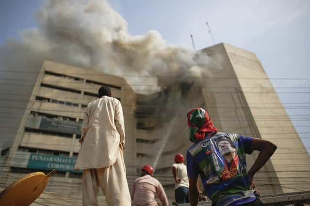 A man (R) with a pre-election poster of Imran Khan, Pakistani cricketer turned politician, watches firefighters trying to put away fire from a burning building in central Lahore May 9, 2013. Fire erupted on the seventh floor of the LDA Plaza in Lahore and quickly spread to higher floors leaving many people trapped inside the building. At least three people fell from the high floors trying to avoid the fire that engulfed the building, local media reports. (Photo by Damir Sagolj/Reuters)
