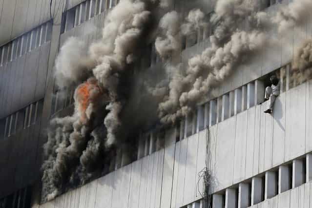 A man sits on the window of a burning building before falling from it, in central Lahore May 9, 2013. Fire erupted on the seventh floor of the LDA plaza in Lahore and quickly spread to higher floors leaving many people trapped inside the building. At least three people fell from the high floors trying to avoid fire that engulfed the building, local media reports. (Photo by Damir Sagolj/Reuters)