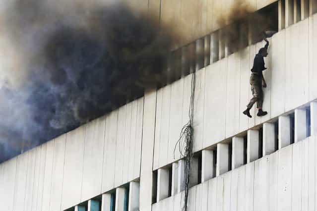 A man falls from a high floor of a burning building in central Lahore May 9, 2013. Fire erupted on the seventh floor of the LDA plaza in Lahore and quickly spread to higher floors leaving many people trapped inside the building. At least three people fell from the high floors trying to avoid fire that engulfed the building, local media reports. (Photo by Damir Sagolj/Reuters)