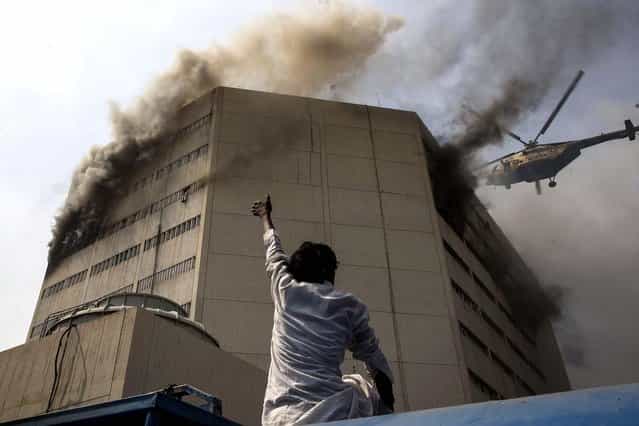 A bystander gestures to a helicopter and points to a man stranded by a fire at the Lahore Development Authority Plaza in Lahore, Pakistan. Helicopters were used to rescue stranded victims from the roof of the building, but at least five people plunged to their deaths from the burning building. (Photo by Daniel Berehulak/Getty Images)