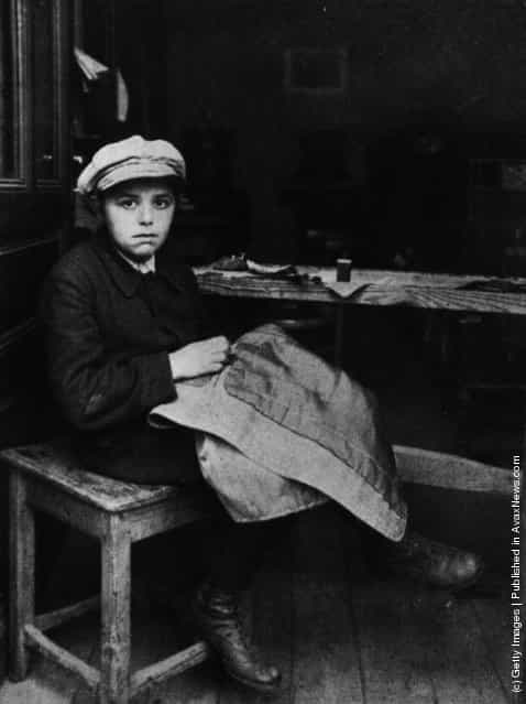 circa 1915: A Jewish boy sewing at his home in East London