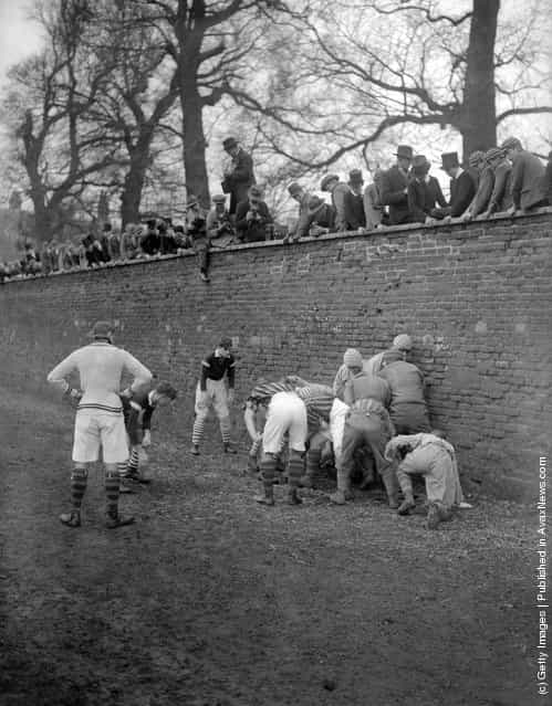 1928: A group of public school boys watch their classmates playing the Eton Wall Game, traditionally played between town and school on St Andrews Day, and unique to Eton