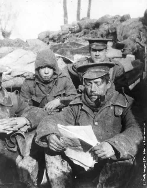 1915: Infantrymen sitting in a trench reading and smoking during the early days of trench warfare in the First World War