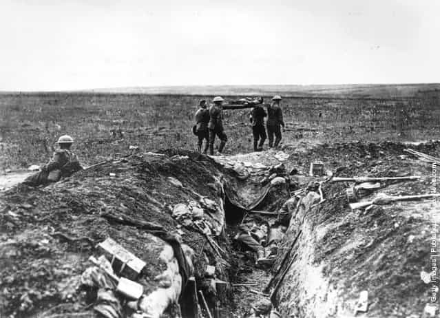1915: A wounded British soldier is stretchered back to camp past a carnage-strewn trench, during the First World War