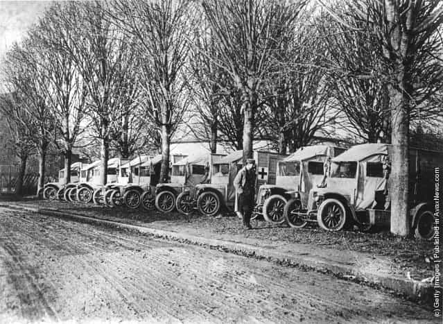 1915: Ambulances during WW I parked under trees on a road in France