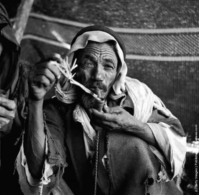 1950: An elderly Arab Bedouin sits loading and smoking a pipe
