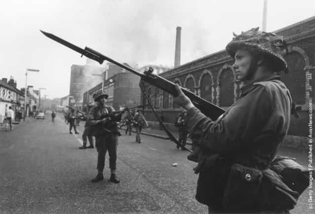 British soldiers on guard duty in the Falls area of Belfast, 1st October 1969. A mill is blazing in the background