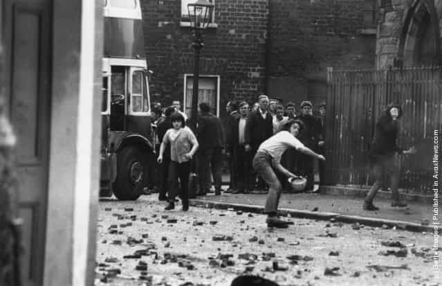 Young men throwing stones at the Royal Ulster Constabulary (RUC) in the Falls Road area of Belfast. Five Catholics were killed, 60 injured and hundreds of homes devastated after armed British soldiers attempted to impose a curfew