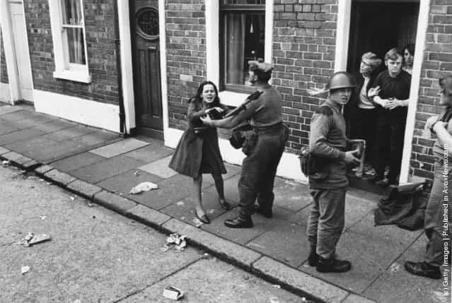 Armed British soldiers restrain a young civilian in the streets of Belfast, 1970