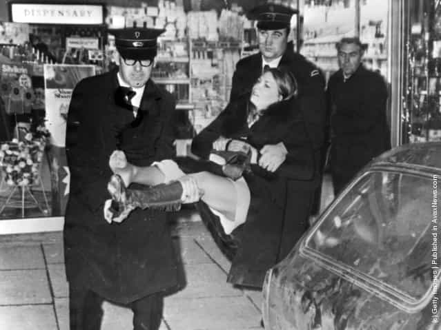 1971: A young woman injured during a shooting incident in Belfast is carried out of a chemists shop by ambulance men