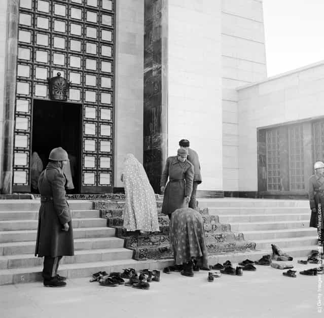 1950: A woman taking off her shoes and leaving them with a pile of others at the entrance to the former Shah of Persias Mausoleum which is guarded by soldiers