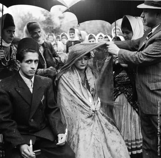 1952: A Khan or feudal lord of a province lifts the veil from the face of a muslim bride in a village wedding ceremony. Her groom sits beside her with lit candles symbolising life
