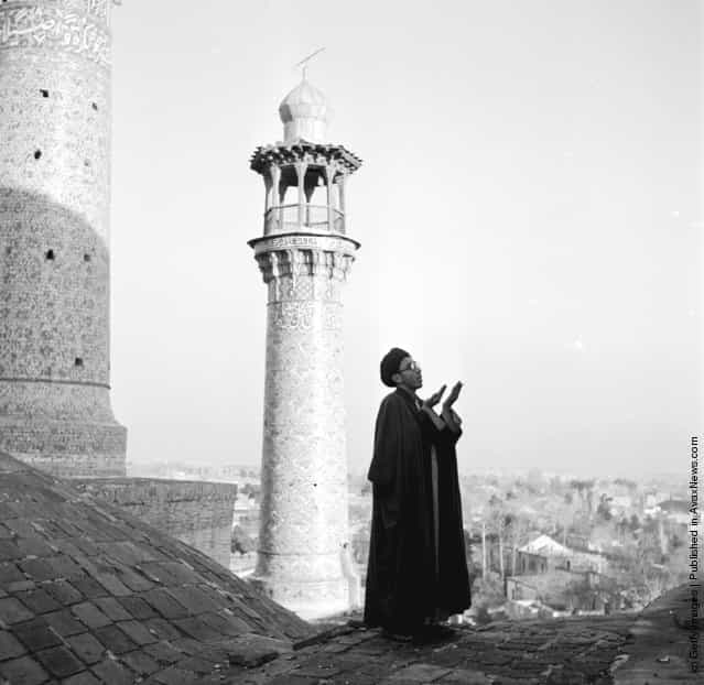 1952: Standing on a rooftop a muezzin is calling the faithful to prayer. Behind him rises a minaret