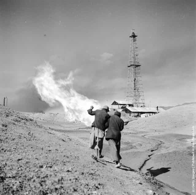 1954: Shielding themselves from the far-reaching heat of a burning oil well, two Iranian National Oil Company workers rush across the fields of the Iranian countryside