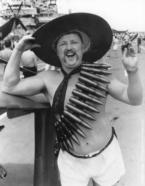 1982: Kenneth Rocky Hudson, a Petty Officer from Gosport aboard HMS Hermes, the flagship of the Royal Navy, heading for the Falkland Islands. The troops are waging a Mexican moustache growing contest and Kenneth is wearing 30mm cannon shells slung around his body and sporting a fat cigar