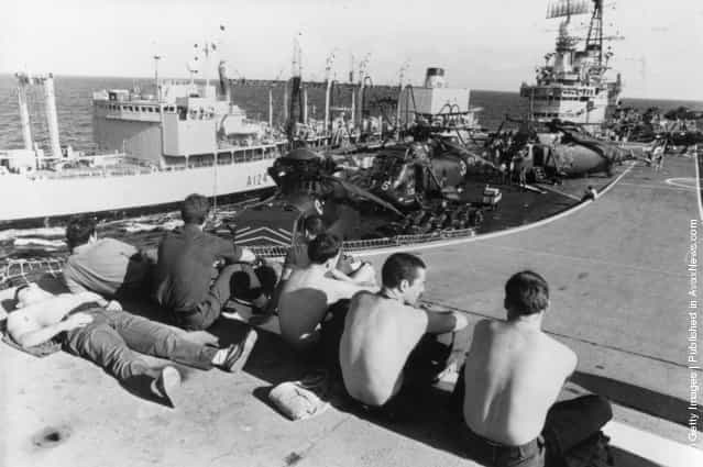 1982: Marines relaxing on the ski jump ramp of HMS Hermes, as she is replenished at sea by a Royal Fleet auxiliary vessel, on the way to the Falkland Islands. Westland Sea King helicopters can be seen on deck