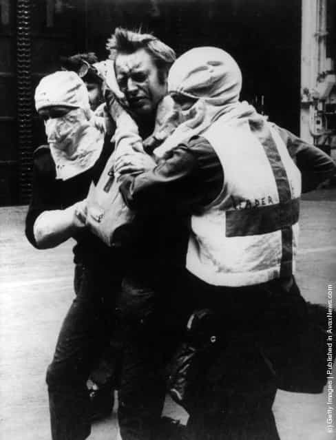 Medical orderlies wearing anti-flash gear tend a wounded survivor of HMS Sheffield aboard HMS Hermes during the Falklands War