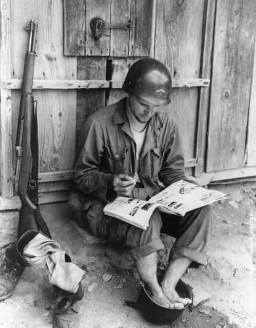 An American soldier relaxes by taking a footbath in a spare helmet whilst reading a magazine, during the Korean War, 1950