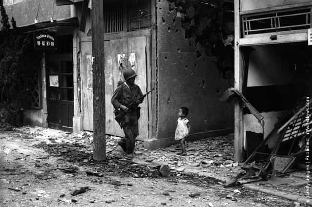 An American soldier patrolling the streets of Inchon after the capture of this key port during the Korean war, is watched by a young Korean child, 1950