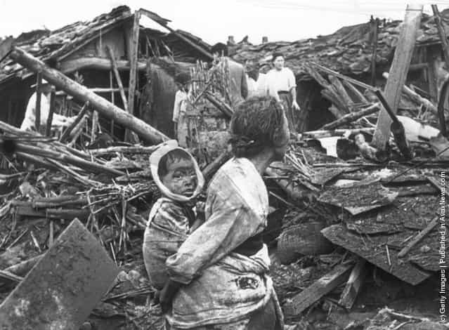 1950: An elderly woman and her grandchild wander among the debris of their wrecked home in the aftermath of an air raid by U.S. planes over Pyongyang, the Communist capital of North Korea