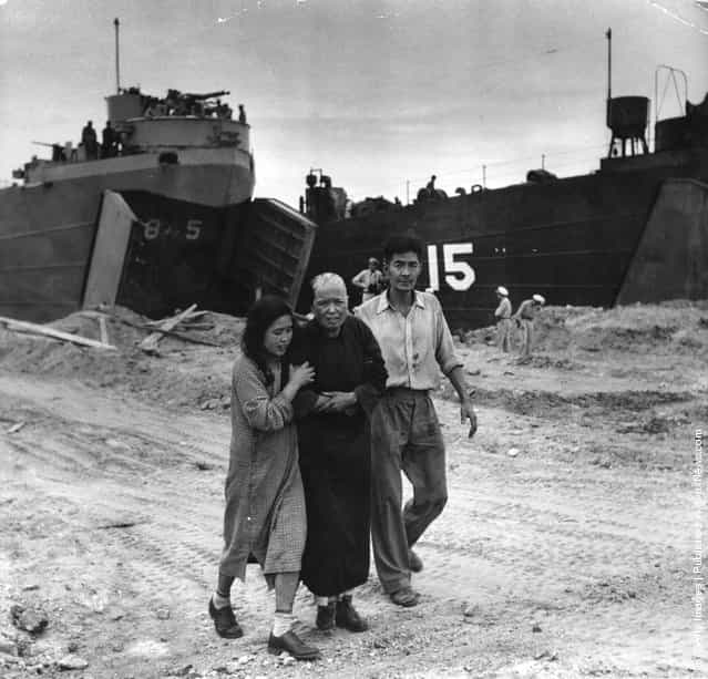 A civilian casualty arrives on the beach at Inchon in South Korea to see the US medical officer during the Korean War. US amphibious craft used in the invasion are in the background