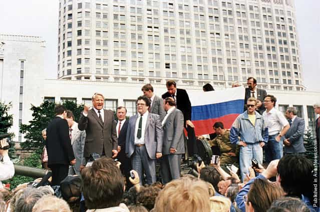 Russian President Boris Yeltsin (left) stands on top of an armored vehicle parked in front of the Russian Federation building as supporters hold a Russian federation flag on August 19, 1991, during a coup attempt. Yeltsin addressed a crowd of supporters calling for a general strike