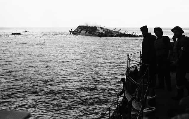 The dramatic scene as the Cunard White Star liner Lancastria was sunk on August 3, 1940. The Lancastria was evacuating British nationals and troops from France, and had boarded as many as possible for the short trip – an estimated 4,000 to 9,000 passengers were aboard. A German Junkers 88 aircraft bombed the ship shortly after it departed, and it sank within twenty minutes. While 2,477 were rescued, an estimated 4,000 others perished by bomb blasts, strafing, drowning, or choking in oil-fouled water. Photo taken from one of the rescue boats as the liner heels over, as men swarm down her sides and swim for safety to the rescue ships. Note the large number of bobbing heads in the water