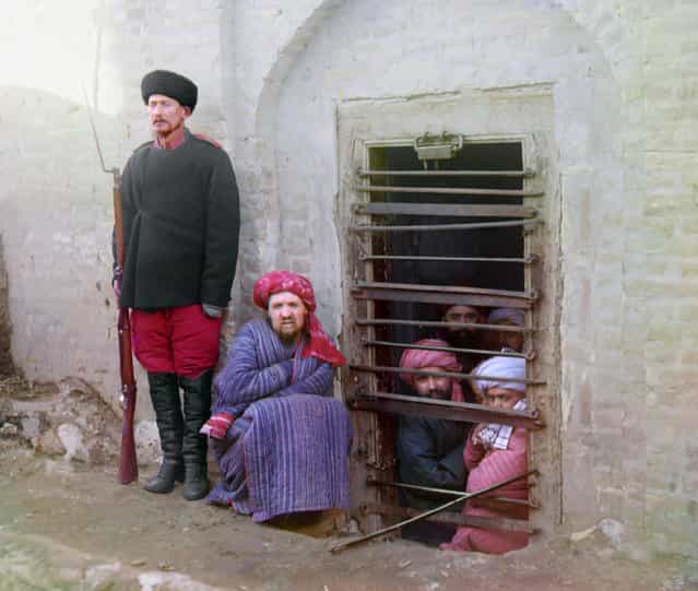 Photos by Sergey Prokudin-Gorsky. Zindan (prison), with inmates looking out through the bars and a guard with Russian rifle, uniform, and boots, Central Asia. Russia, Emirate of Bukhara, Bukhara area, 1907