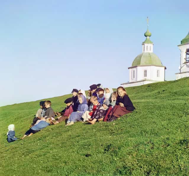 Photos by Sergey Prokudin-Gorsky. Russian children sitting on the side of a hill near a church and bell tower in the countryside near White Lake, in the north of European Russia. The picture was taken at the church in the background Pyatnitskaya Belozersk (not preserved). Novgorod Province, White Lake County, 1909