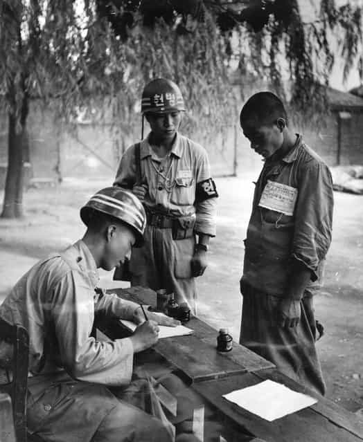 A North Korean prisoner of war being registered by a member of the South Korean forces at a POW camp at Taegu during the Korean War, 1950. (Photo by Bert Hardy)