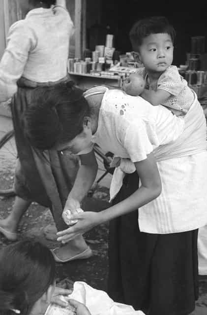 A Korean refugee mother carries her child on her back through the streets of Pusan, the United Nations communications centre during the Korean war, 1950. (Photo by Bert Hardy)