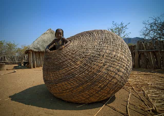 [Mundimba tribe girl in giant basket – Angola. Those giant baskets are used to keep the grains in Mundimba tribe, in south Angola]. (Eric Lafforgue)