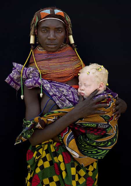 [Albino baby girl and her Mwila mother – Angola. This mwila tribewoman was in Hale and came to me, showing a blue cap coming out from her clothes. i first did not understood there was a baby under this cap. Then she opened her clothes to let appear this albino baby girl. She had some little dreadlocks and was incredibly white. The mother was proud to pause for the picture and discovered the magic of polaroid! I have seen many albinos people in Angola, in the tribes. They are mainly in very bad health, as the sun is very hot there... Perhaps the most moving picture i ever took as the future of this albino baby is not the happiest you can get in this remote area of Africa]. (Eric Lafforgue)