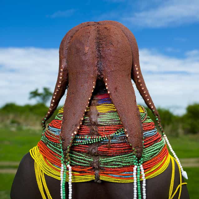 [Paul the Octopus haircut in Mwila tribe – Angola. Mwila (or Mwela, Mumuhuila, or Muhuila) women are famous for their very special hairstyles. Hairstyles are very important and meaningful in Mwila culture. Women coat their hair with a red paste called, oncula, which is made of crushed red stone. They also put a mix of oil, crushed tree bark, dried cow dung and herbs on their hair. Besides they decorate their hairstyle with beads, cauri shells (real or plastic ones) and even dried food. Shaving the forehead is considered as a sign of beauty. The plaits, which look like dreadlocks, are called nontombi and have a precise meaning. Women or girls usually have 4 or 6 nontombi, but when they only have 3 it means that someone died in their family. Mwila Women are also famous for their necklaces, which are central and meaningful as for each period of their life corresponds a specific type of necklace. Young girls wear necklaces, heavy red made with beads covered with a mix of soil land latex. Later girls wear yellow necklaces called, Vikeka, made with wicker covered with earth. They keep until their wedding which can last 4 years. When married they start to wear a set of stacked up bead necklaces, called Vilanda. Women never take their necklace off and have to sleep with it. They also use headrests to protect their hairstyles. However, more and more men and women dress in a western way, because people make fun of them when they go to markets. Women sometimes walk 50 kilometers to sell goods in Huila market. Mwila rarely eat meat, they rather eat porridge, corn, chicken, honey and milk. They kill their cattle only on special occasions. Mwila are not allowed to mention people’s name in public]. (Eric Lafforgue)