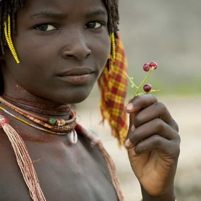 [Mucubal tribe girl – Angola. Mucubal like to eat this kind of cranberries. They boil them. To know if the water is hot enough, she put her hand inside. Once it really hurts, she throw the Cranberries inside. After 1 minute, they eat them. It is like eating some red pepper!]. (Eric Lafforgue)