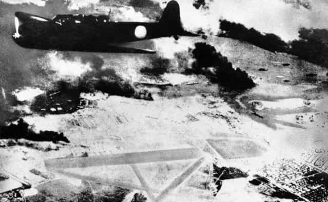 A Japanese bomber on a run over Pearl Harbor, Hawaii is shown during the surprise attack of December 7, 1941. Black smoke rises from American ships in the harbor. Below is a U.S. Army air field. (Photo by Associated Press)