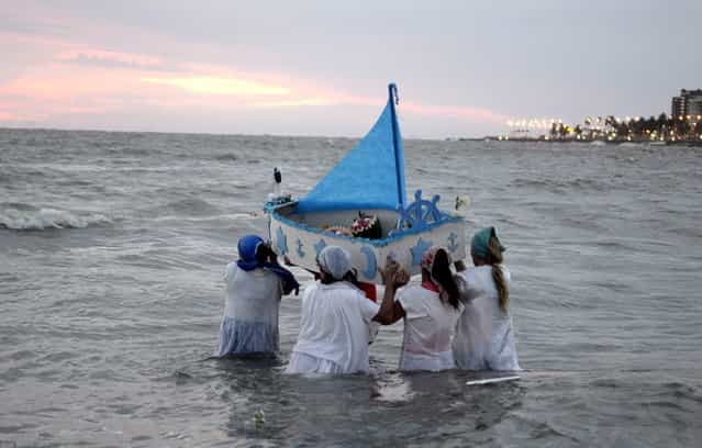 Faithful carry a boat out to sea, filled with offerings to Yemanja, the African sea goddess, during a ceremony honoring the deity in Montevideo, Uruguay, Saturday, February 2, 2013. Thousands of worshippers come to the beach in Montevideo on her feast day, February 2, bearing candles, flowers, perfumes and fruit to show their gratitude for her blessings bestowed upon them. The belief in the goddess sprouts from Umbanda, a blend of religions that include African, Catholicism and Spiritism. (Photo by Matilde Campodonico/AP Photo)