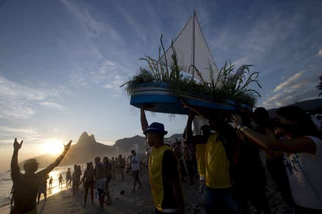 Simpatia e Quase Amor or [Kindness is almost love], block party members and faithful carry a boat filled with flowers as an offering to the sea goddess,Yemanja, during a pre-Carnival celebration in Rio de Janeiro, Brazil, Saturday, February 2, 2013. Worshippers honor the deity, offering flowers and launching boats, large and small, into the ocean showing their gratitude for her blessings bestowed upon them. The belief in the goddess comes from the African Yoruban religion brought to America by West African slaves. (Photo by Silvia Izquierdo/AP Photo)