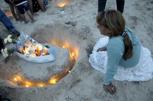 A woman prepares an offering for Yemanja, the African sea goddess, during a ceremony honoring the deity in Montevideo, Uruguay, Saturday, February 2, 2013. Thousands of worshippers come to the beach in Montevideo on her feast day, February 2, bearing candles, flowers, perfumes and and fruit to show their gratitude for her blessings bestowed upon them. The belief in the goddess sprouts from Umbanda, a blend of religions that include African, Catholicism and Spiritism. (Photo by Matilde Campodonico/AP Photo)