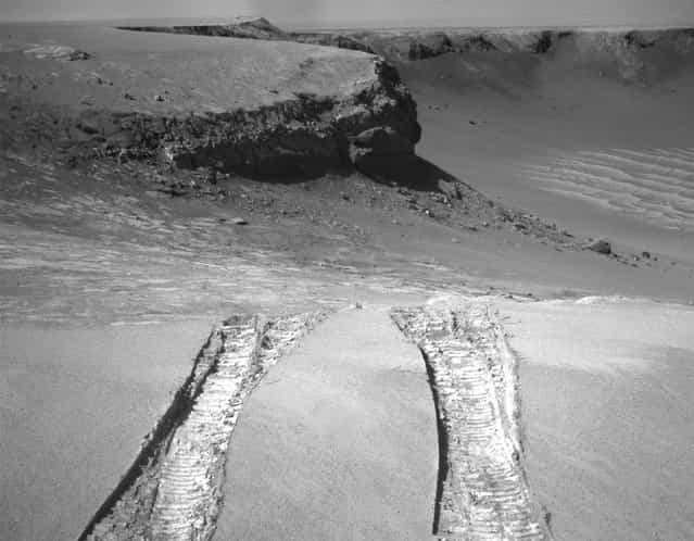 Opportunity climbs out of Victoria Crater on August 28, 2008, following the tracks it had made when it descended into the 800-meter-diameter (half-mile-diameter) bowl nearly a year earlier. The rover's navigation camera captured this view back into the crater just after finishing a 6.8-meter (22-foot) drive that brought Opportunity out onto level ground during the mission's 1,634th Martian day, or sol. (Photo by AP Photo/NASA/The Atlantic)