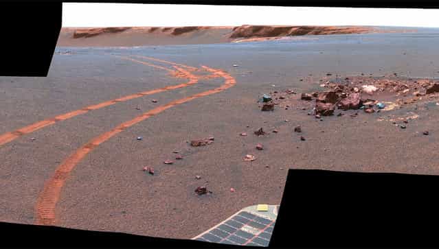 This view from Opportunity shows the tracks left by a drive executed with more onboard autonomy than has been used on any other drive by a Mars rover. Opportunity made the curving, 15.8-meter (52-foot) drive during its 1,160th Martian day, or sol (April 29, 2007). It was testing a navigational capability called [Field D-star], which enables the rover to plan optimal long-range drives around any obstacles in order to travel the most direct safe route to the drive's designated destination. Victoria Crater is in the background, at the top of the image. (Photo by NASA/JPL-Caltech/Cornell University/The Atlantic)