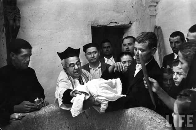 While his godfather holds him over a font, the priest Don Manuel dries the head of month-old Buenaventura Jimenez Morena after his baptism at village church. (Photo by W. Eugene Smith/Time & Life Pictures)