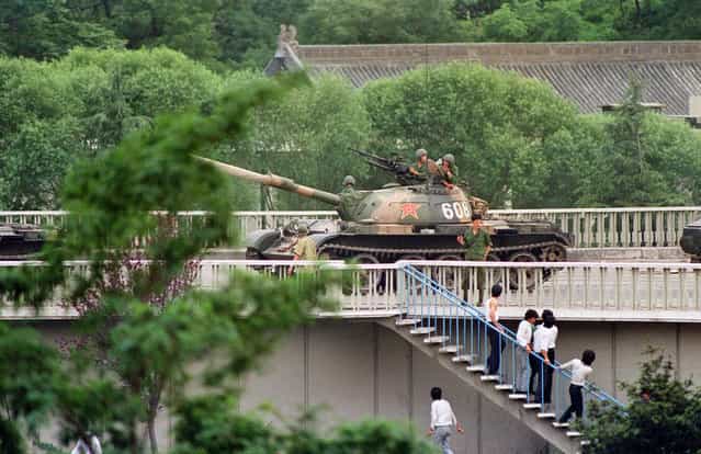 Chinese onlookers run away as a soldier threatens them with a gun on June 5, 1989 as tanks took position at Beijing's key intersections next to the diplomatic compound. (Photo by Catherine Henriette/AFP Photo)