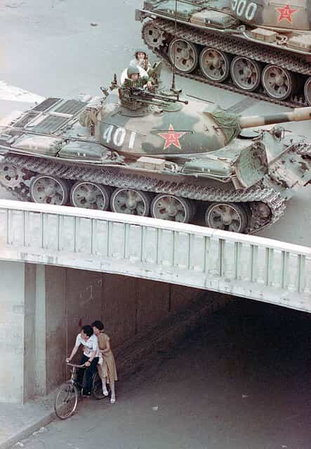 A Chinese couple on a bicycle take cover beneath an underpass as tanks deploy overhead in eastern Beijing, on June 5, 1989. (Photo by Liu Heung Shing/AP Photo)